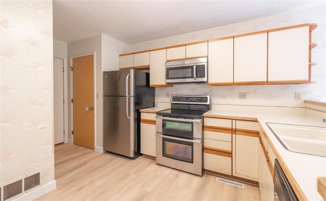 kitchen with light hardwood / wood-style floors, a textured ceiling, sink, white cabinets, and stainless steel appliances