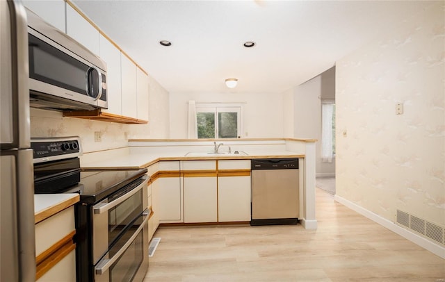 kitchen with white cabinetry, sink, light wood-type flooring, kitchen peninsula, and stainless steel appliances