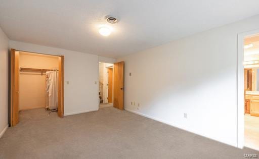 unfurnished bedroom featuring a closet, light colored carpet, connected bathroom, and a spacious closet