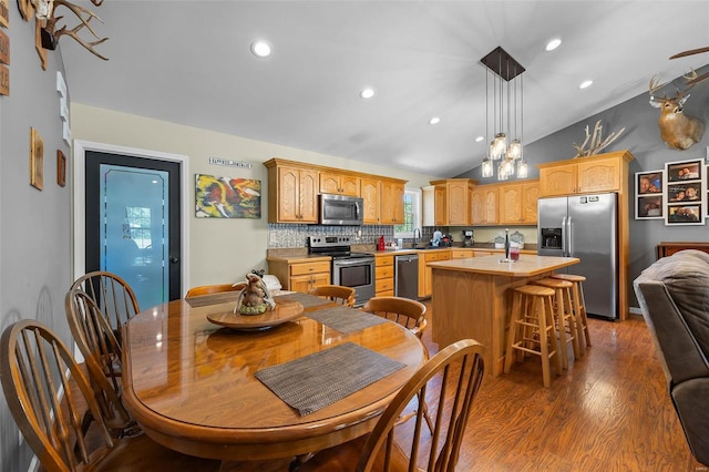 kitchen featuring vaulted ceiling, appliances with stainless steel finishes, tasteful backsplash, an island with sink, and dark wood-type flooring