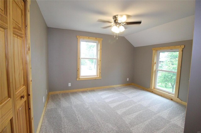 carpeted empty room featuring ceiling fan, vaulted ceiling, and plenty of natural light