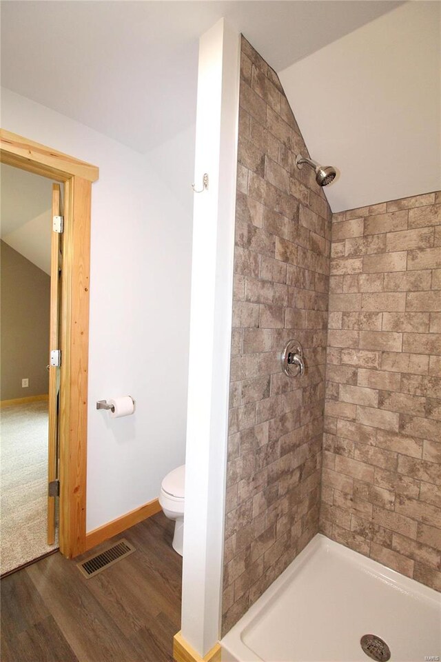 bathroom with toilet, a tile shower, wood-type flooring, and vaulted ceiling