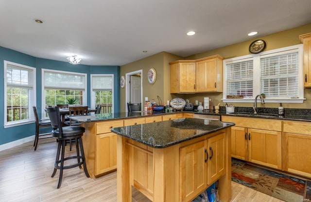 kitchen with dark stone counters, sink, light brown cabinets, a kitchen island, and light wood-type flooring