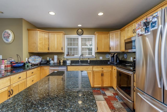 kitchen with appliances with stainless steel finishes, sink, light brown cabinets, dark stone countertops, and wood-type flooring