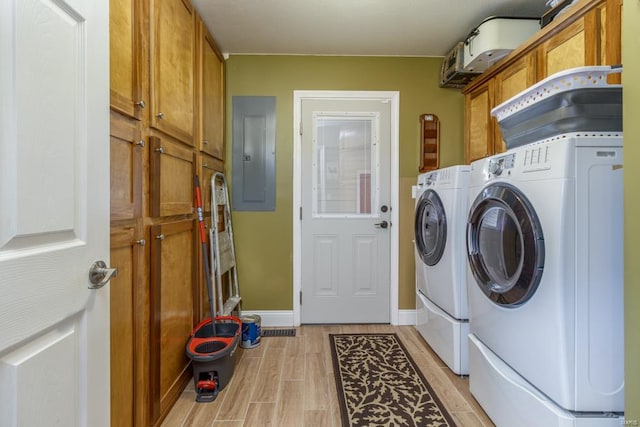 clothes washing area featuring washing machine and dryer, light hardwood / wood-style flooring, cabinets, and electric panel