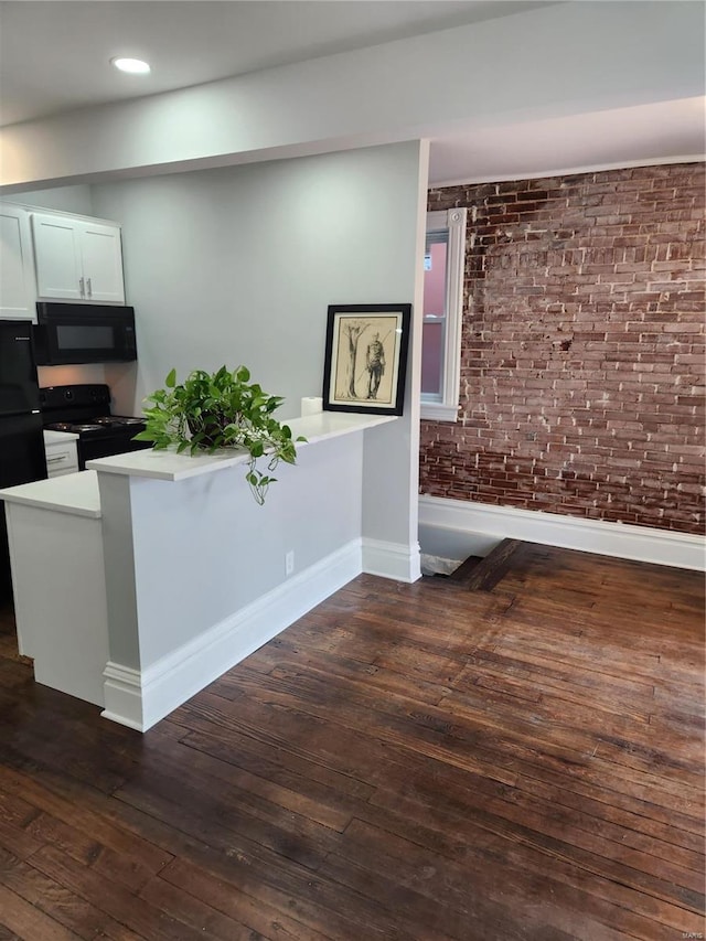 interior space featuring kitchen peninsula, dark hardwood / wood-style flooring, brick wall, black appliances, and white cabinetry