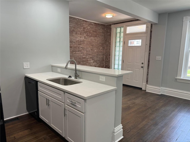 kitchen with sink, black dishwasher, brick wall, kitchen peninsula, and white cabinets