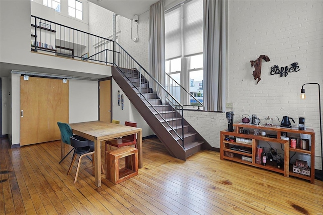 dining area with a towering ceiling, wood-type flooring, and brick wall