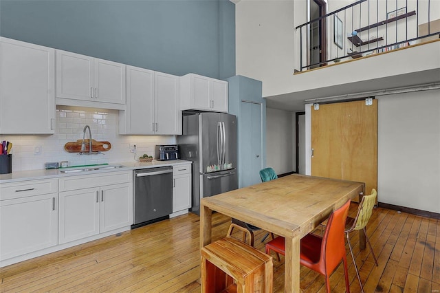 kitchen featuring sink, white cabinetry, light hardwood / wood-style flooring, a towering ceiling, and stainless steel appliances