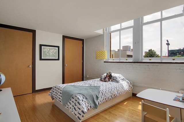 bedroom featuring multiple windows, light hardwood / wood-style floors, and brick wall