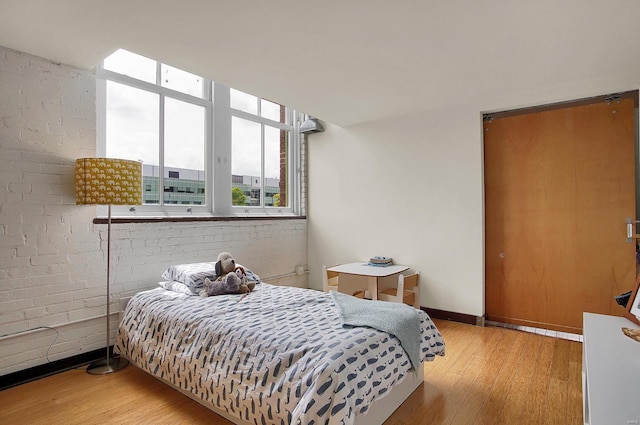 bedroom with brick wall and light hardwood / wood-style floors