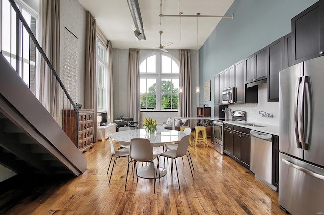 dining space featuring ceiling fan, a towering ceiling, sink, and light wood-type flooring