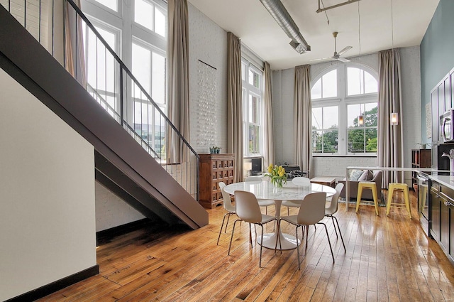 dining area with hardwood / wood-style flooring, a towering ceiling, ceiling fan, and brick wall