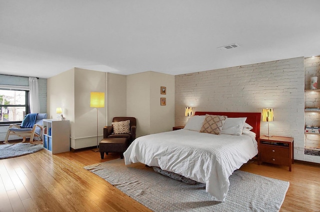 bedroom with brick wall and light hardwood / wood-style floors