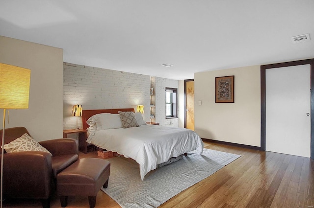 bedroom featuring brick wall and wood-type flooring