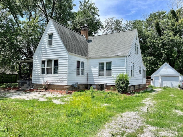 rear view of property with a lawn, a garage, and an outbuilding