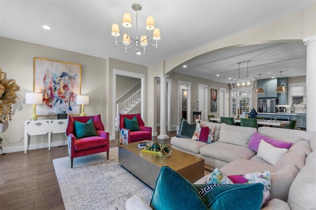 living room featuring a chandelier, arched walkways, wood finished floors, stairway, and ornate columns