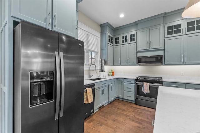 kitchen featuring gray cabinetry, a sink, appliances with stainless steel finishes, dark wood finished floors, and glass insert cabinets