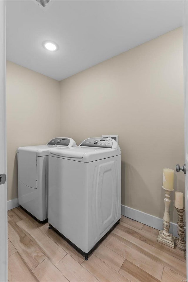 laundry area with light wood-type flooring, laundry area, washing machine and dryer, and baseboards