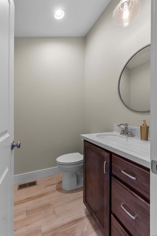 half bath with visible vents, toilet, vanity, wood finished floors, and baseboards