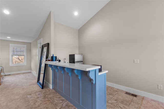 kitchen featuring visible vents, lofted ceiling, a breakfast bar, a peninsula, and light countertops