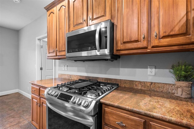 kitchen with appliances with stainless steel finishes, tile patterned flooring, and dark stone counters