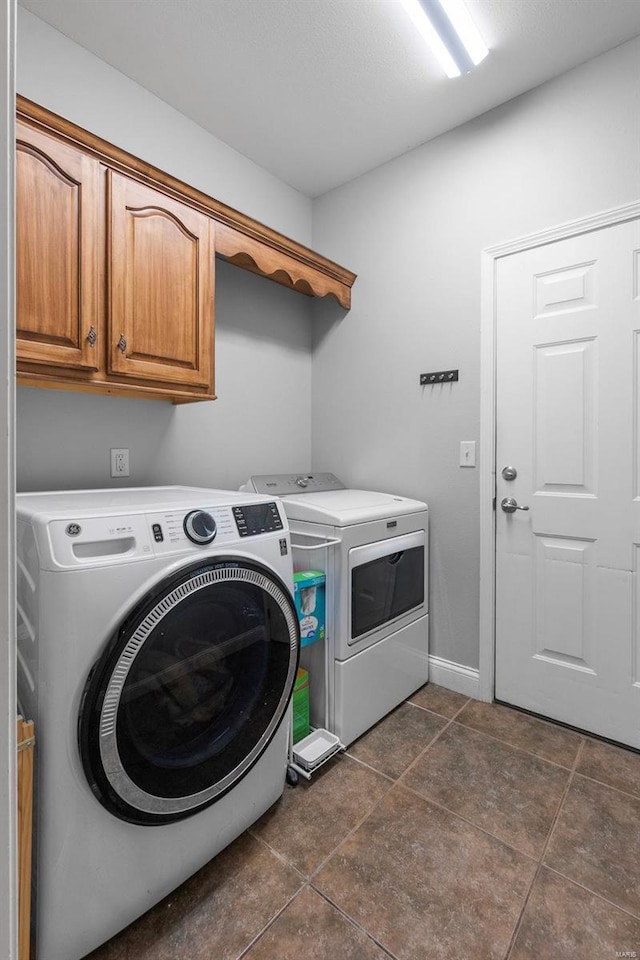 clothes washing area with washing machine and clothes dryer, cabinets, and dark tile patterned flooring