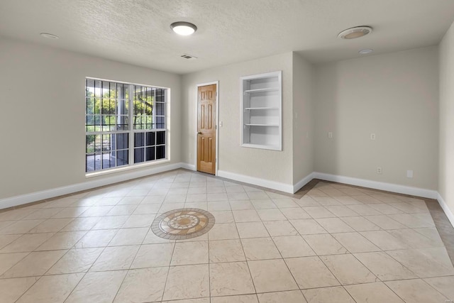 empty room featuring built in features, light tile patterned flooring, and a textured ceiling