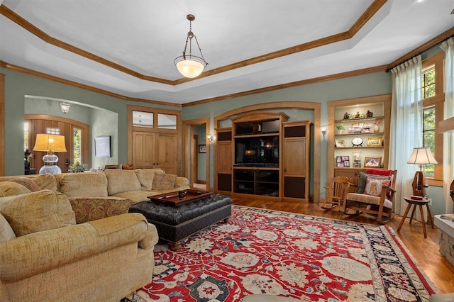 living room with ornamental molding, a raised ceiling, hardwood / wood-style flooring, and built in features