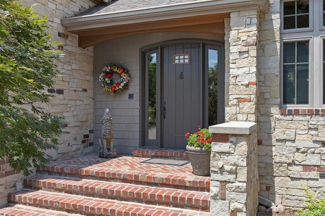 entrance to property featuring a porch, stone siding, and roof with shingles