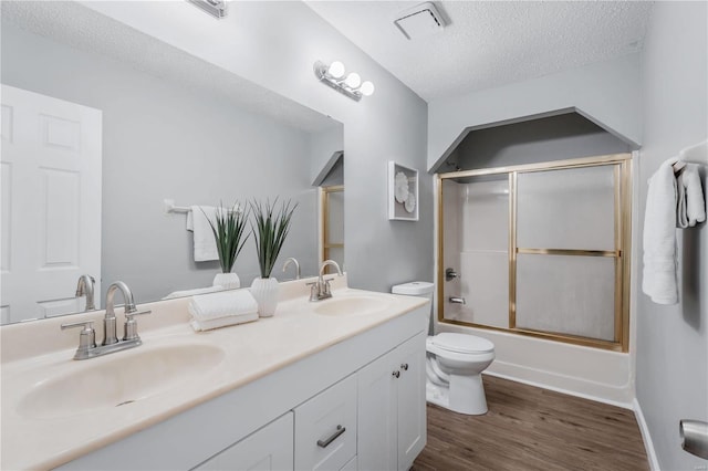 full bathroom with combined bath / shower with glass door, vanity, a textured ceiling, hardwood / wood-style floors, and toilet