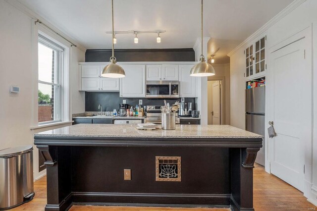 kitchen with light stone counters, a kitchen island, track lighting, appliances with stainless steel finishes, and decorative light fixtures