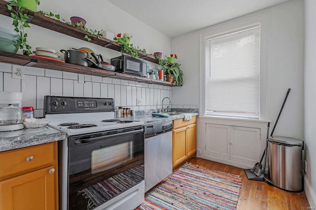 kitchen with electric range, dishwasher, light hardwood / wood-style floors, light stone countertops, and sink