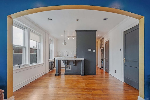 kitchen with a breakfast bar area, decorative light fixtures, a kitchen island, crown molding, and light wood-type flooring