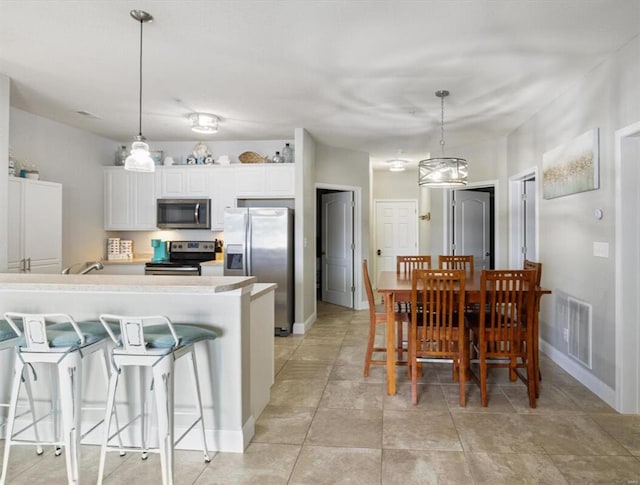 kitchen with light tile patterned flooring, pendant lighting, stainless steel appliances, and white cabinetry