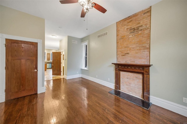 unfurnished living room with dark wood-type flooring, brick wall, and ceiling fan