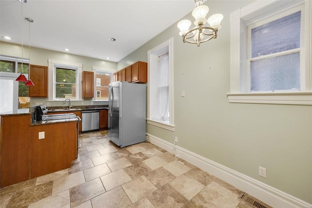 kitchen with pendant lighting, sink, stainless steel appliances, a notable chandelier, and dark stone counters