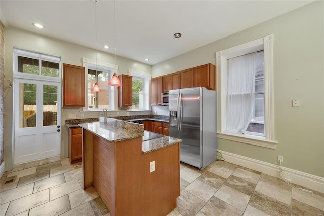 kitchen with appliances with stainless steel finishes, hanging light fixtures, a kitchen island, and dark stone countertops