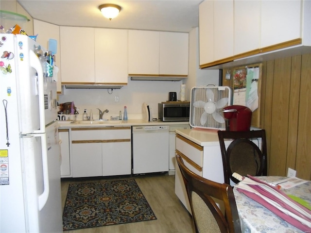 kitchen with wood walls, hardwood / wood-style floors, sink, white appliances, and white cabinets