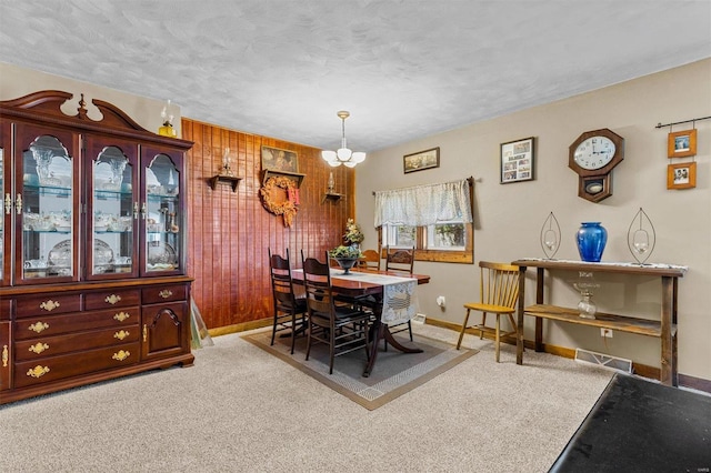 dining space with a notable chandelier, carpet flooring, and wooden walls