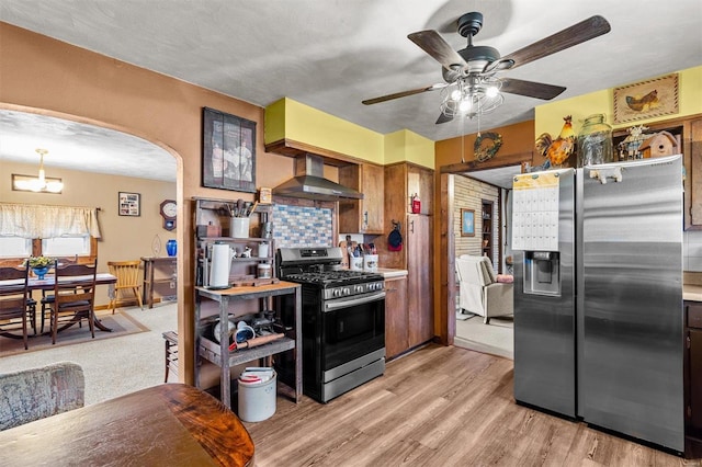 kitchen with stainless steel appliances, wall chimney range hood, backsplash, ceiling fan with notable chandelier, and light carpet