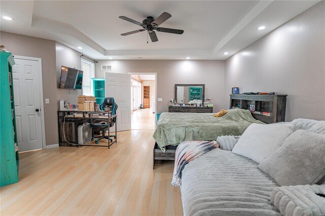 bedroom featuring a raised ceiling, ceiling fan, and light wood-type flooring