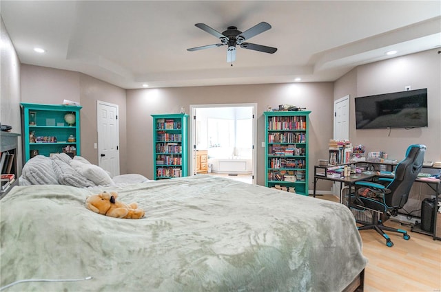 bedroom with hardwood / wood-style floors, a tray ceiling, ensuite bath, and ceiling fan