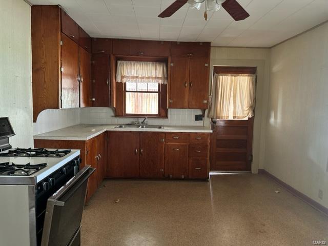 kitchen with a sink, baseboards, range with gas stovetop, light countertops, and tasteful backsplash