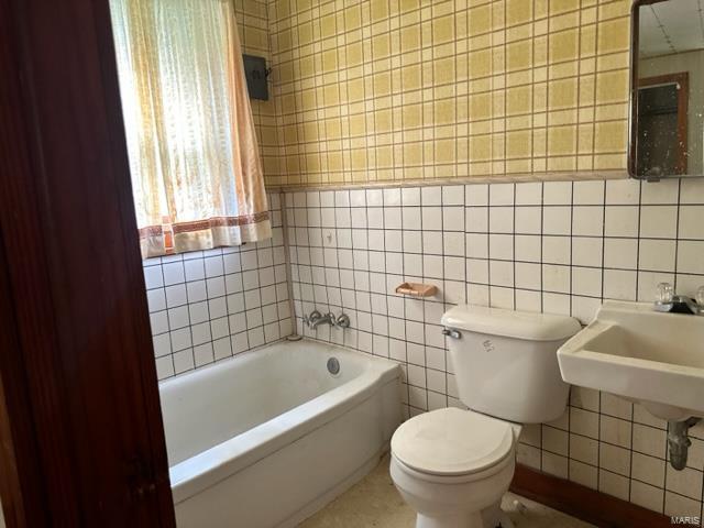 full bathroom featuring toilet, a tub to relax in, and tile walls