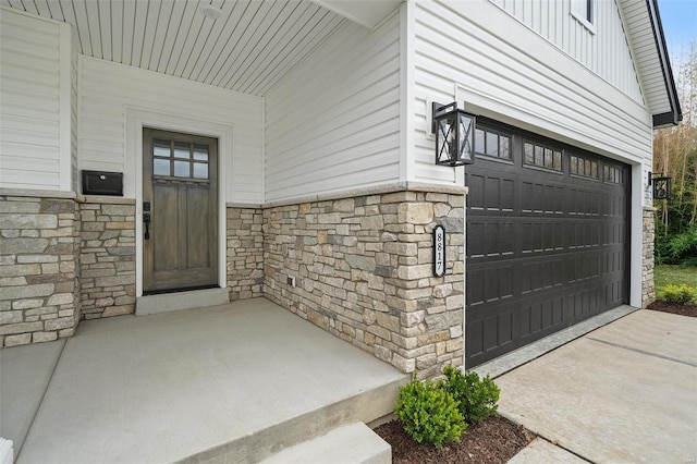 doorway to property featuring board and batten siding, stone siding, and concrete driveway