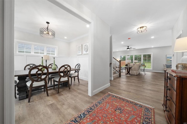 dining room with a decorative wall, recessed lighting, wood finished floors, stairs, and crown molding