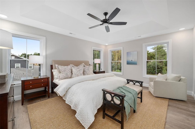 bedroom featuring light wood-type flooring, baseboards, a raised ceiling, and a ceiling fan