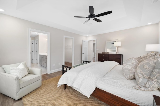 bedroom with a closet, a raised ceiling, a spacious closet, wood finished floors, and baseboards