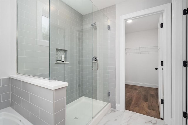 bathroom with marble finish floor, a spacious closet, a shower stall, baseboards, and a bath